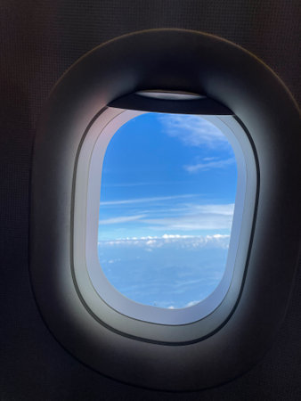 Looking out through the airplane window at the beautiful blue sky and sunlit white fluffy clouds. Smartphone photographyの写真素材