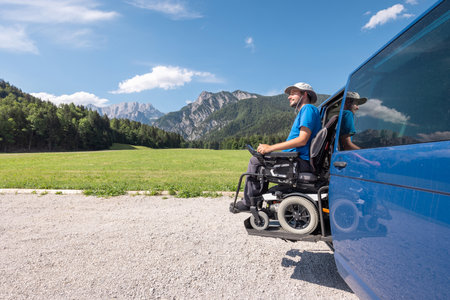 Young Caucasian man in a wheelchair using the vertical platform lift to get in the van parked in the natureの写真素材