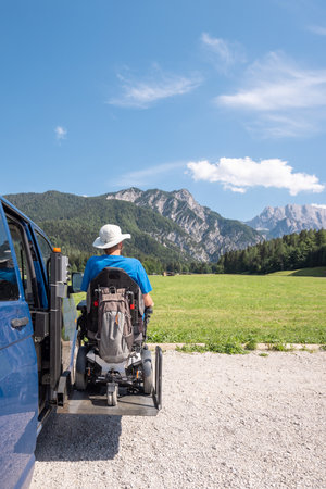Man with disability using hydraulic wheelchair lift to get in the van, after a summer day spent on beautiful mountain natureの写真素材