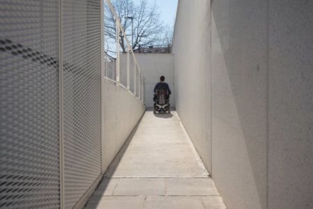 Man on wheelchair, approaching the building moving along an accessible ramp for persons with disabilityの写真素材
