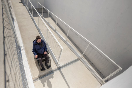 Man on wheelchair, approaching the building moving along an accessible ramp for persons with disabilityの写真素材