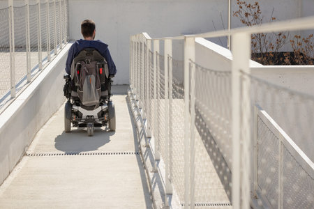 Man on wheelchair, approaching the building moving along an accessible ramp for persons with disabilityの写真素材