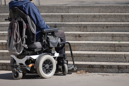 Man with disability on wheelchair stopped in front of staircase, raising awareness of architectural barriers and accessibility issuesの写真素材