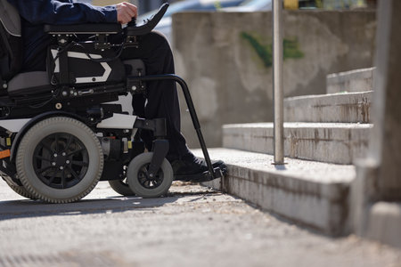 Person with disability on electric wheelchair stopping at the bottom of inaccessible staircase,...