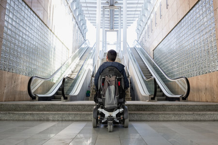 Person with disability on electric wheelchair stopping at the bottom of staircase, unable to reach the topの写真素材