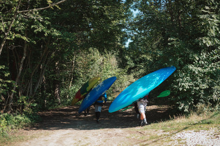 Three Caucasian recreational sportsmen going down to the river carrying kayaks and paddlesの写真素材