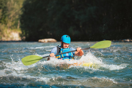 Caucasian man skillfully steering kayak in the river, crossing over whitewater rapidsの写真素材
