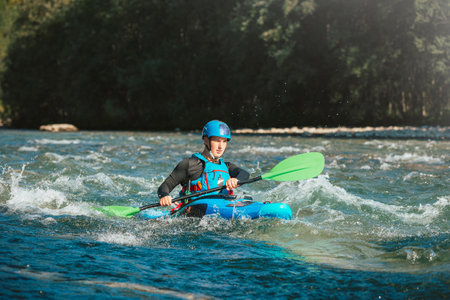 Male recreational athlete paddling carefully over the risky, foamy, and splashy whitewater rapids in his blue kayakの写真素材