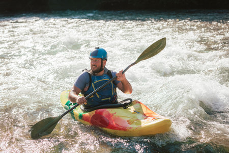Caucasian man kayaking over the mountain river rapids, with the beautiful rocky bank and green forest in the background. Water sportの写真素材