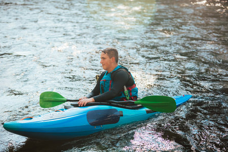 Male recreational athlete paddling carefully over the risky, foamy, and splashy whitewater rapids in his blue kayakの写真素材