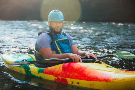 Caucasian man kayaking over the mountain river rapids, with the beautiful rocky bank and green...