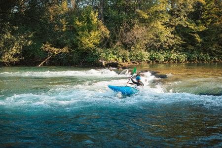 Young teenager cruising down whitewater rapids in a blue kayak, beautiful river nature on a sunny summer day, handheld shot.の写真素材