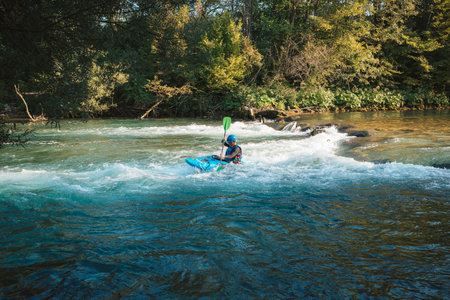 Male recreational athlete paddling carefully over the risky, foamy, and splashy whitewater rapids in his blue kayakの写真素材