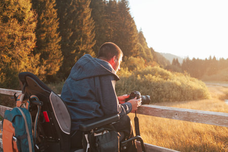 Young Caucasian man on wheelchair on a wooden bridge, using a camera to take a photo of beautiful mountain natureの写真素材