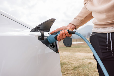 Male hand putting a charger in electric car socket, in the background visible mountain natureの写真素材
