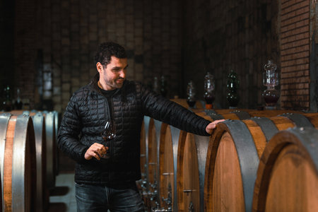 Man in the wine cellar with barrels in background drinking and tasting wine.の写真素材