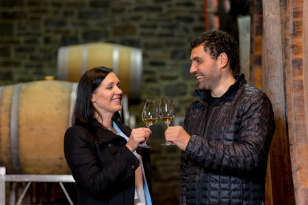 Couple in the wine cellar, enjoying drinking white wine while looking at old wooden barrels for wine...