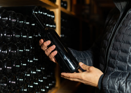 Man in the wine cellar with bottles in background drinking and tasting wine.
