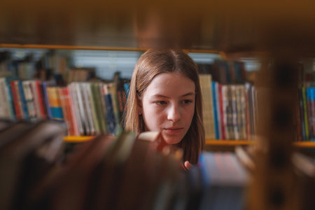 Teenage girl taking a book from a bookshelf in the school library. Education learning concept.