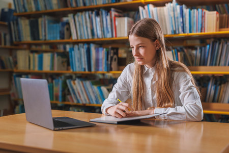 Academic teen girl studying in the library, solving assignments, writing and erasing answers in a...