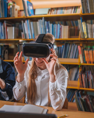 Girl student using modern tech devices in the library, a laptop and VR headset. Concepts of virtual reality experience in education.の写真素材