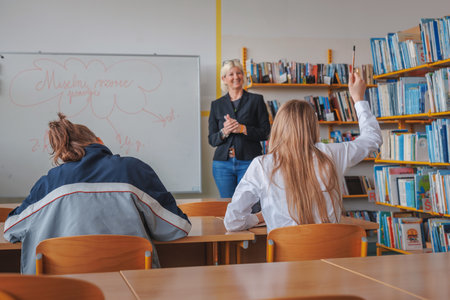 Girl students raising their hands during classroom instruction, communicating with smiling female teacherの写真素材