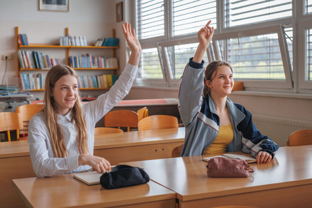 Two teen female pupils raising their hands to answer the question in the classroom. Back to school...