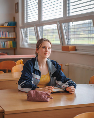 Teenage schoolgirl sitting at a school desk in the classroom and listening to the teacher