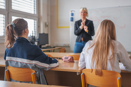 Rear view of two female students during a lecture in the classroom, looking at female teacher teachingの写真素材