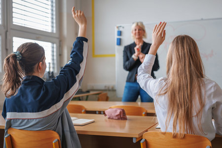 Female student raising her hand and answering a cheerful smiling teacher's question. Motivation, education, and class activity concepts.の写真素材
