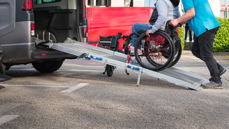 Person on wheelchair with disability using accessible car ramp for transport with help of an...