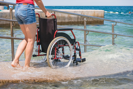 Woman assistant pushing wheelchair at sea on accessible beach with ramp for persons with disabilityの写真素材