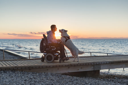 Man with disability with his service dog at sunset using electric wheelchair.の写真素材