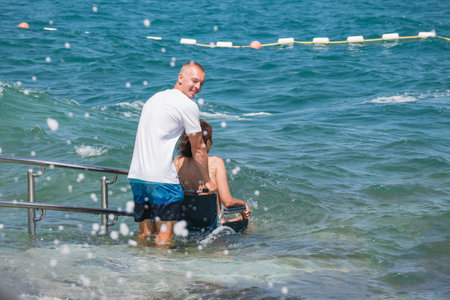 Woman with disability on wheelchair at accessible beach goes swimming.の写真素材