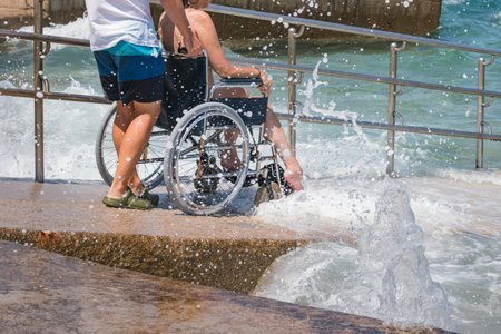 Man with disability on wheelchair at accessible beach goes swimming.