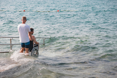 Man with disability on wheelchair at accessible beach goes swimming.の写真素材