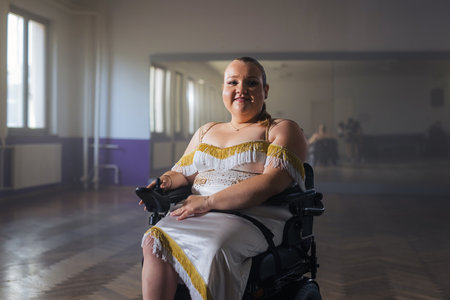 Confident pretty young woman with a disability, on her electric wheelchair in a dance hall, looking and smiling at a camera, inspiration portrait.の写真素材
