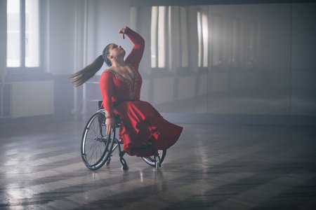 Young beautiful woman in a red dress dancing in a wheelchair, enjoying elegant graceful movements and agile whirls.の写真素材