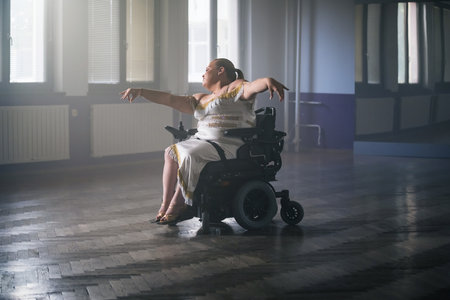 Female dancer, an electric wheelchair user performing graceful dance moves during training in a ballroom.の写真素材
