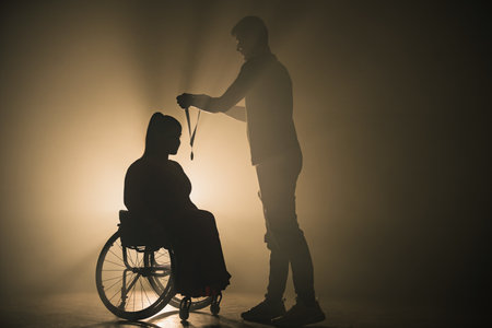 Woman in a wheelchair receiving a medal from a man on a dark stage under a spotlight. Success, victory, and disability concept.の写真素材
