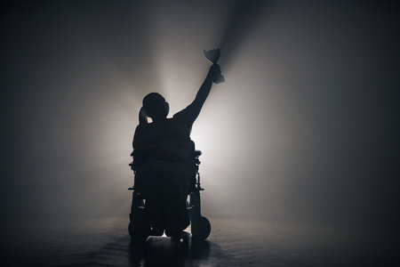Woman with disability receiving a victory cup while sitting in a wheelchair in a dark room with one white backlight.の写真素材