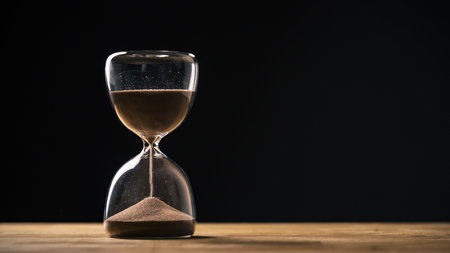Sandglass on a black background, flowing golden sand grains falling on a pile, close up shot....