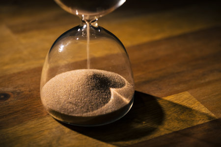 Sandglass on a black background, flowing golden sand grains falling on a pile, close up shot....
