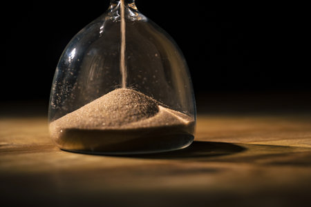Golden glittering sand grains flowing in an hourglass, macro view. Material, texture, and abstract...
