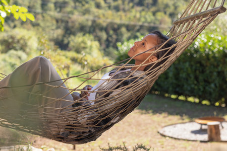 Young African American woman enjoying the tranquility of nature, gently swaying and relaxing in a hammock. Weekend getaway concepts.の写真素材