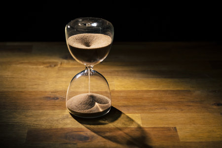 Hourglass on a wooden table with a black background, sand flowing through the bulb. Time, and life...