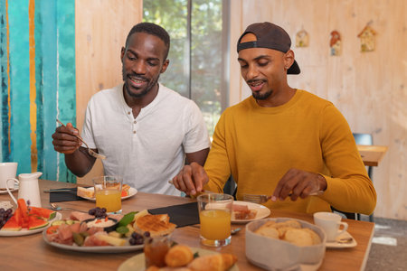 Two African American LGBT couple having breakfast, tasting fresh fruit and vegetables, enjoying delicious healthy food taste in a hotel accommodation.の写真素材