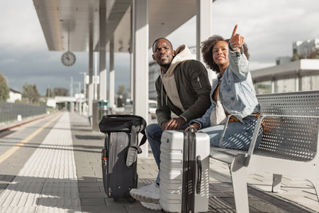 Smiling passengers, a couple waiting for a train to arrive on a railroad platform, excited about their upcoming travel.の写真素材
