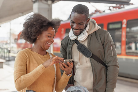 Embraced couple with a suitcases on a railway platform, checking trip informations on a smartphone...