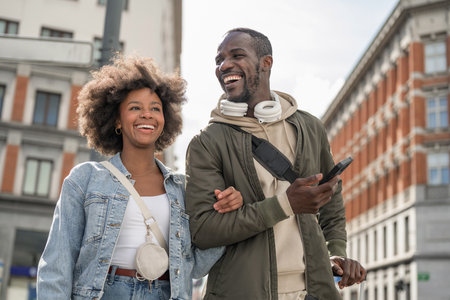 African American traveler couple standing on a street, using smartphones to navigate urban space. Mobile technology and travel concepts.の写真素材